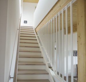 Geschlossene Treppe aus Eichenholz mit weiß lasierten Trittstufen, deckend weiß lackierten Wangen und Geländer