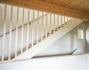 Geschlossene Treppe aus Eichenholz mit weiß lasierten Trittstufen, deckend weiß lackierten Wangen und Geländer